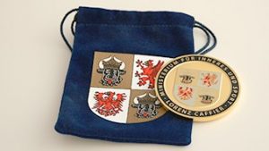 La pièce et son sachet en velours bleu, tous les deux avec le blason de la région.